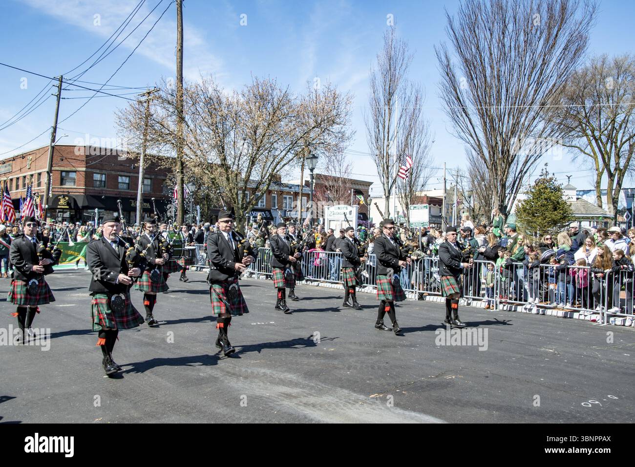 Lindenhurst, New York, États-Unis, 30 mars 2024 - un groupe de cornayeurs portant des kilts écossais traditionnels et des vestes noires défilent dans Une rue ensoleillée pendant Banque D'Images