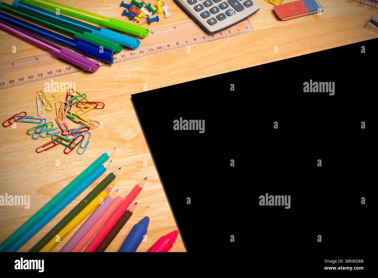 La conception plate montre un bureau en bois avec des surligneurs, des marqueurs, une calculatrice, des crayons et une tablette noire Banque D'Images