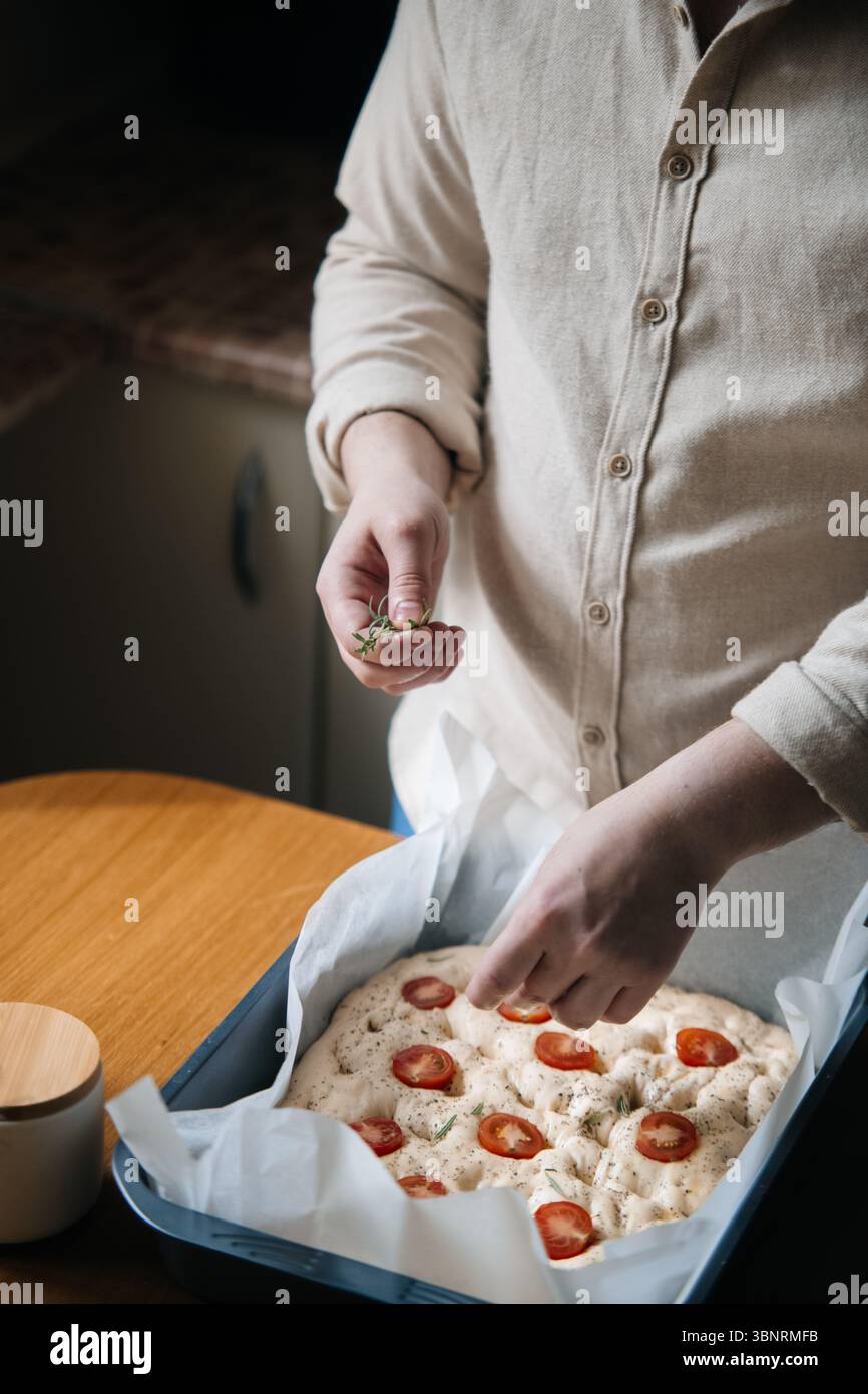 Homme façonnant la pâte focaccia et nappant au romarin Banque D'Images