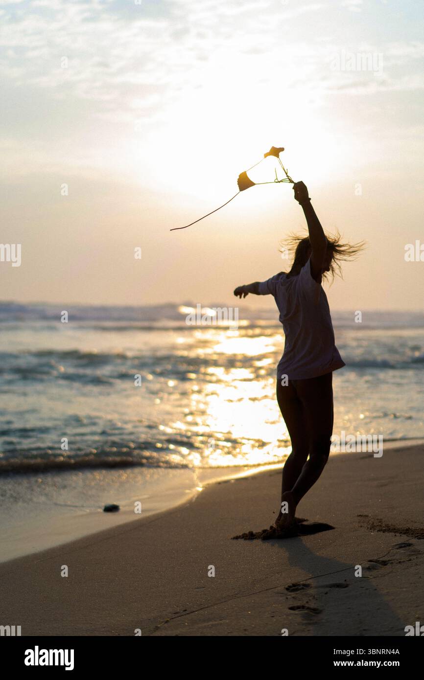 Femme dansant sur la plage au coucher du soleil tenant haut de bikini Banque D'Images