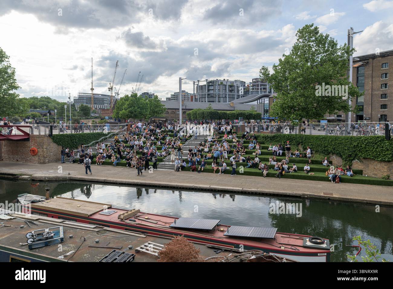Royaume-Uni, Londres, 09 juillet 2025. Les gens se rassemblent sur les marches étagées de Granary Square à King's Cross, profitant de l'espace extérieur sous une spectaculaire Banque D'Images