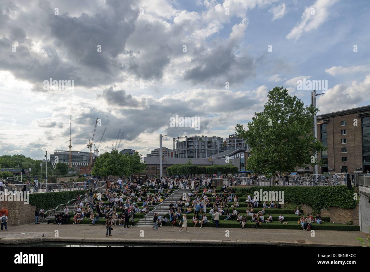 Royaume-Uni, Londres, 09 juillet 2025. Les gens se rassemblent sur les marches étagées de Granary Square à King's Cross, profitant de l'espace extérieur sous une spectaculaire Banque D'Images