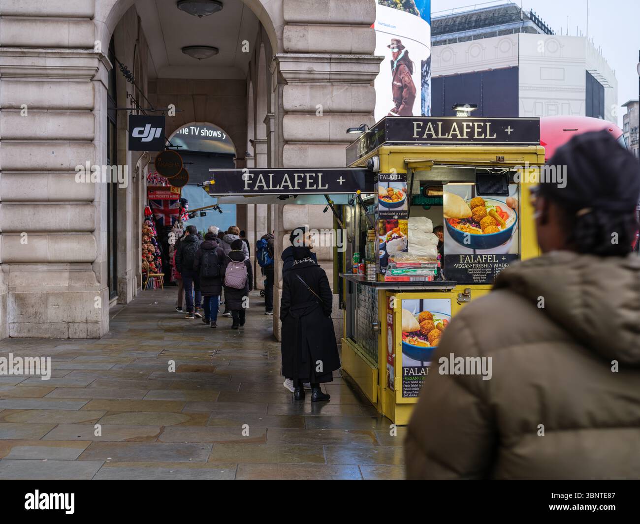 Royaume-Uni, Londres, 8 mars 2023. Un kiosque de rue Falafel+ jaune vif sert les clients le long d'un trottoir animé de Westminster sous les colonnades historiques Banque D'Images