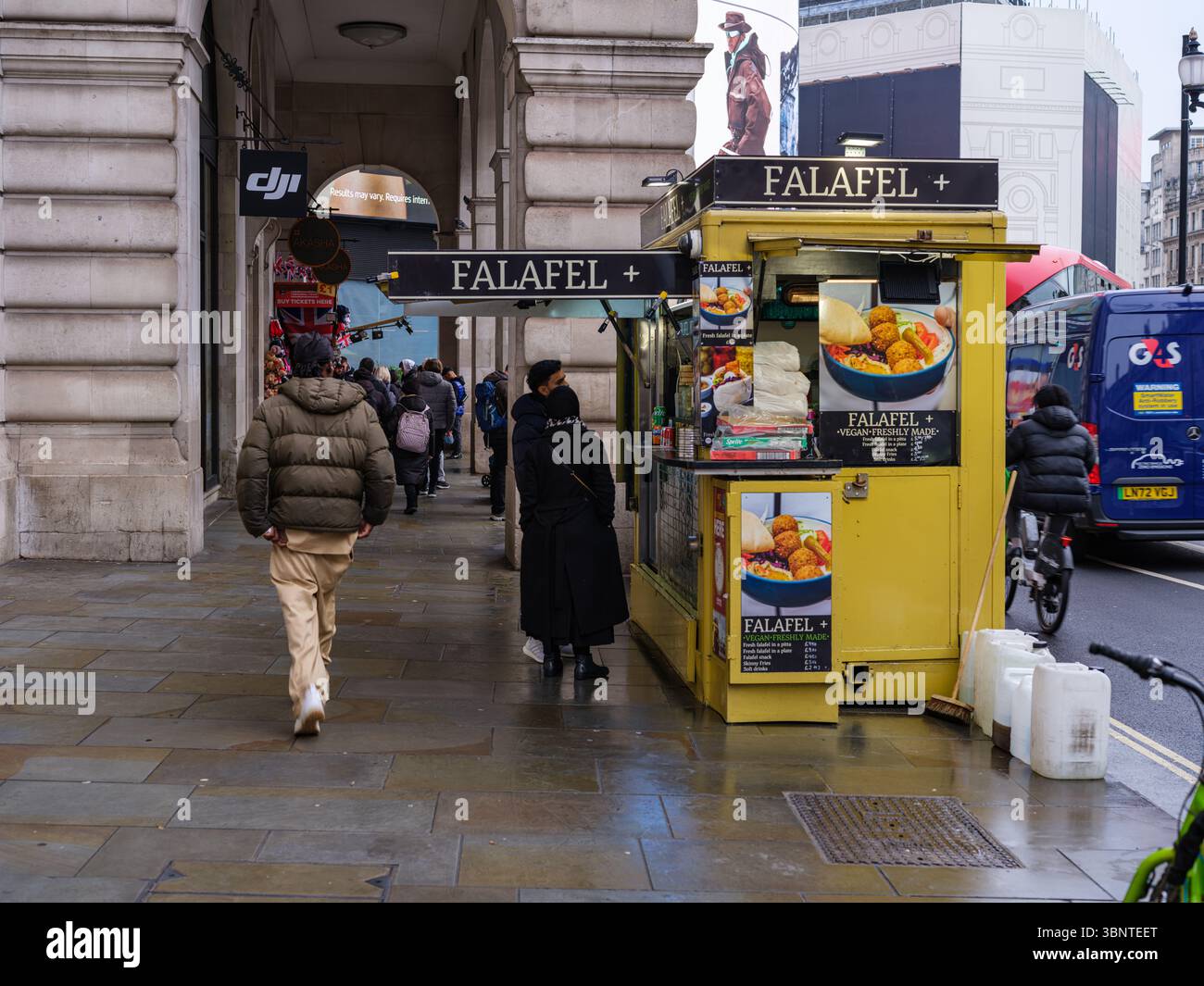 Royaume-Uni, Londres, 8 mars 2023. Un kiosque de rue Falafel+ jaune vif sert les clients le long d'un trottoir animé de Westminster sous les colonnades historiques Banque D'Images