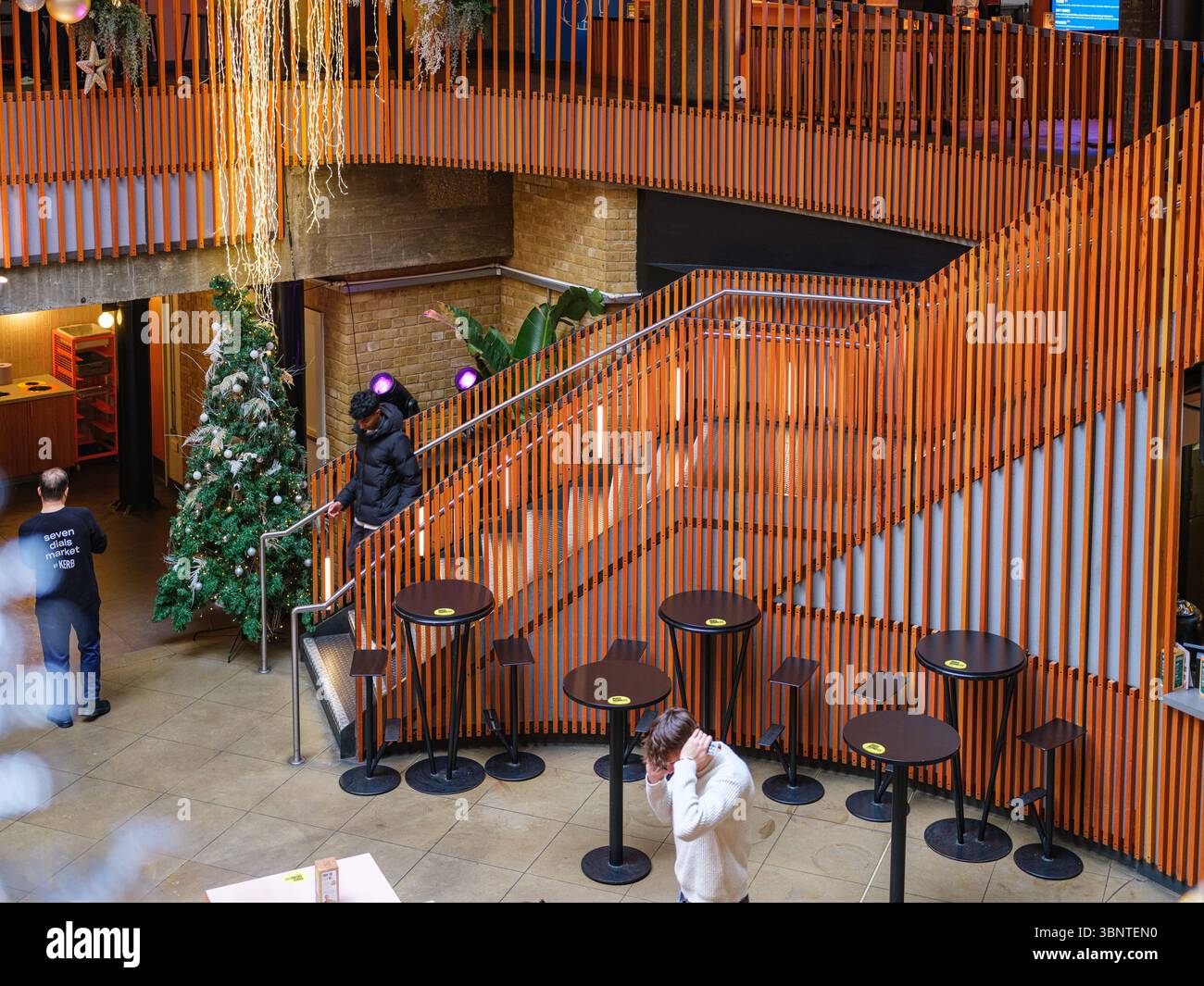 Royaume-Uni, Londres, 2 décembre 2022. Un atrium lumineux est agrémenté d'un superbe escalier de balustrade en bois orange, de tables de café et d'un sapin de Noël festif sous un M. Banque D'Images