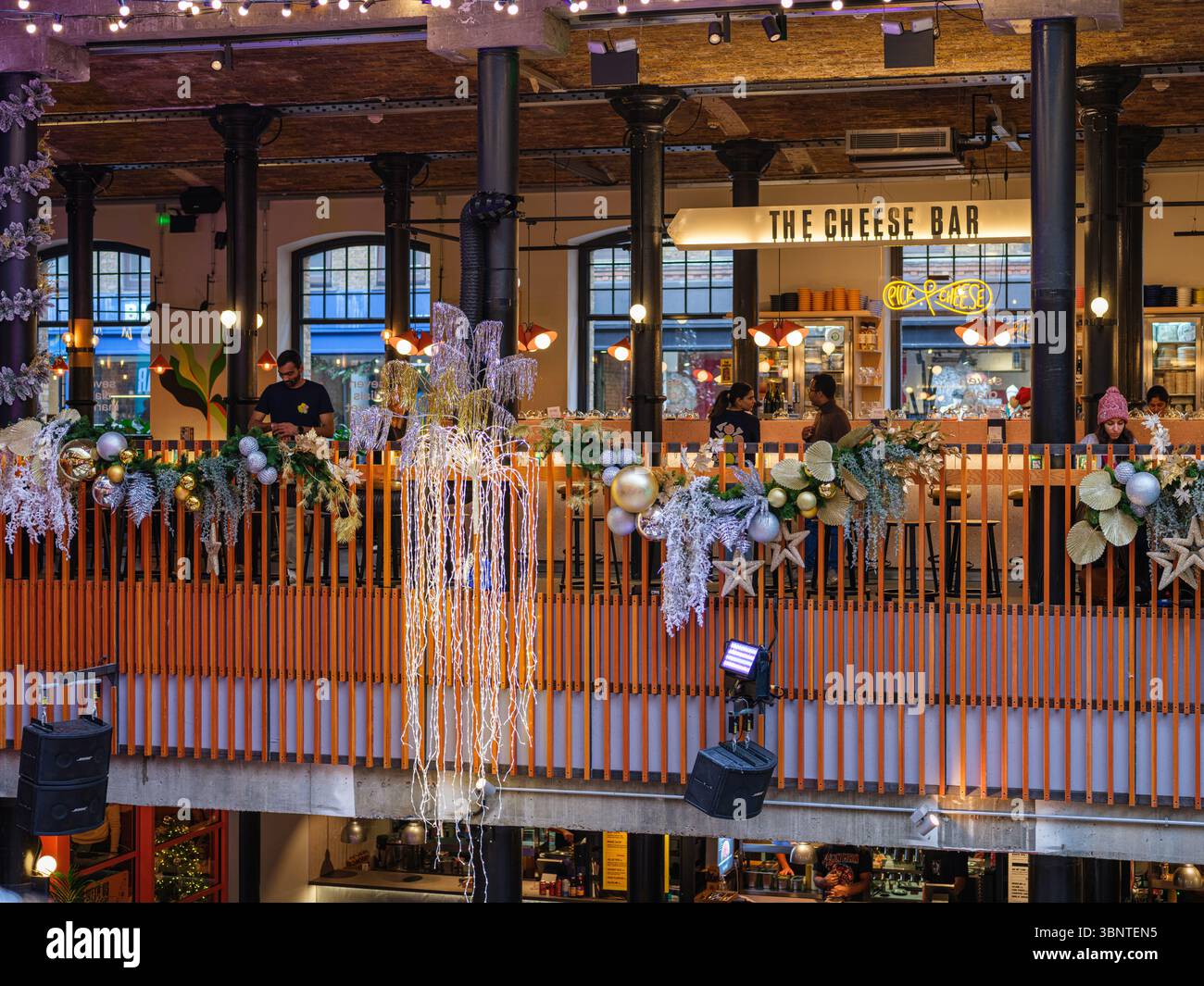 Royaume-Uni, Londres, 2 décembre 2022. Un atrium lumineux est agrémenté d'un superbe escalier de balustrade en bois orange, de tables de café et d'un sapin de Noël festif sous un M. Banque D'Images