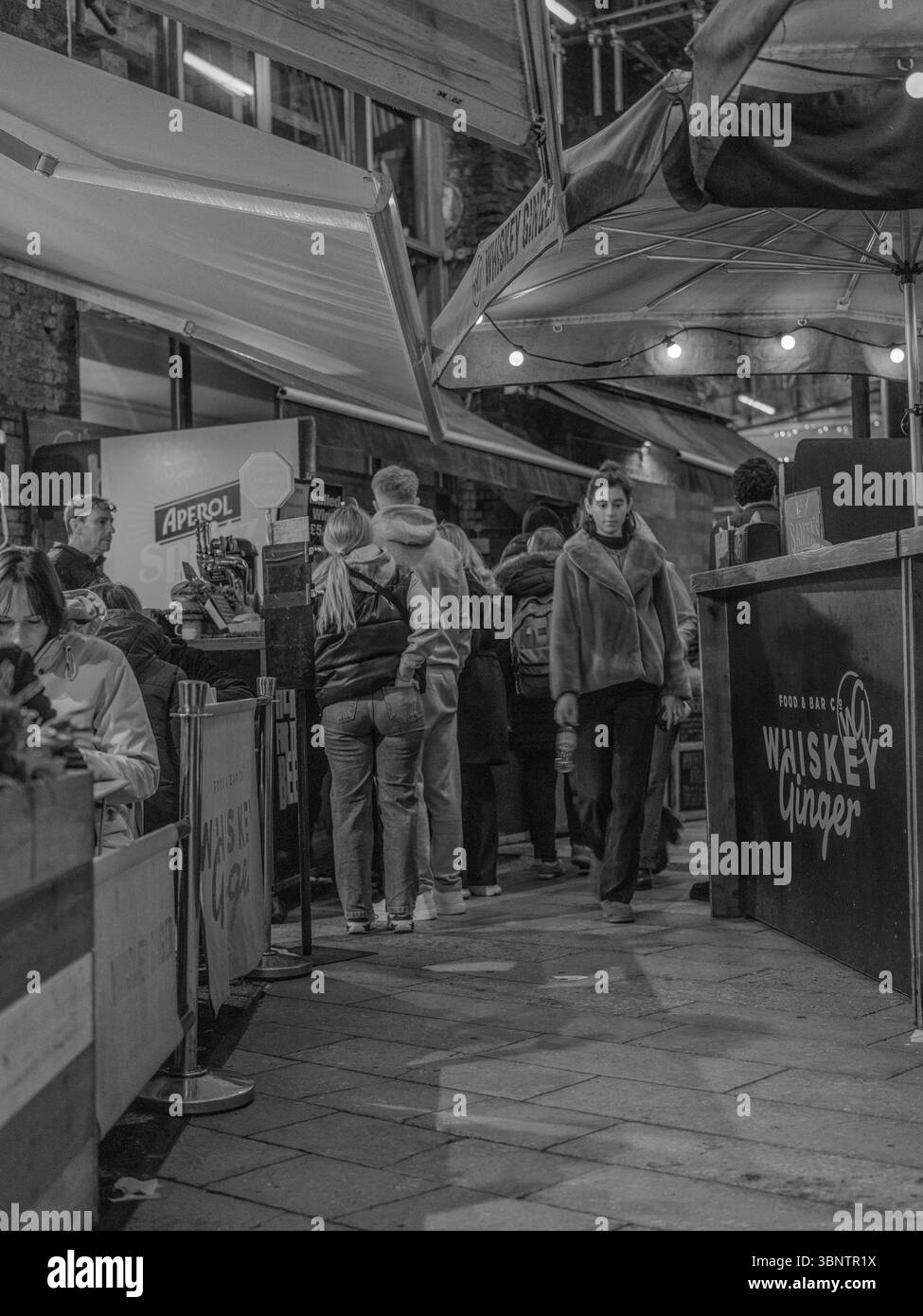 Royaume-Uni, Londres, 11 décembre 2024. Les clients font la queue à un stand de nourriture du marché de Noël dans le centre de Londres, sous les lumières festives et un guichet automatique saisonnier Banque D'Images