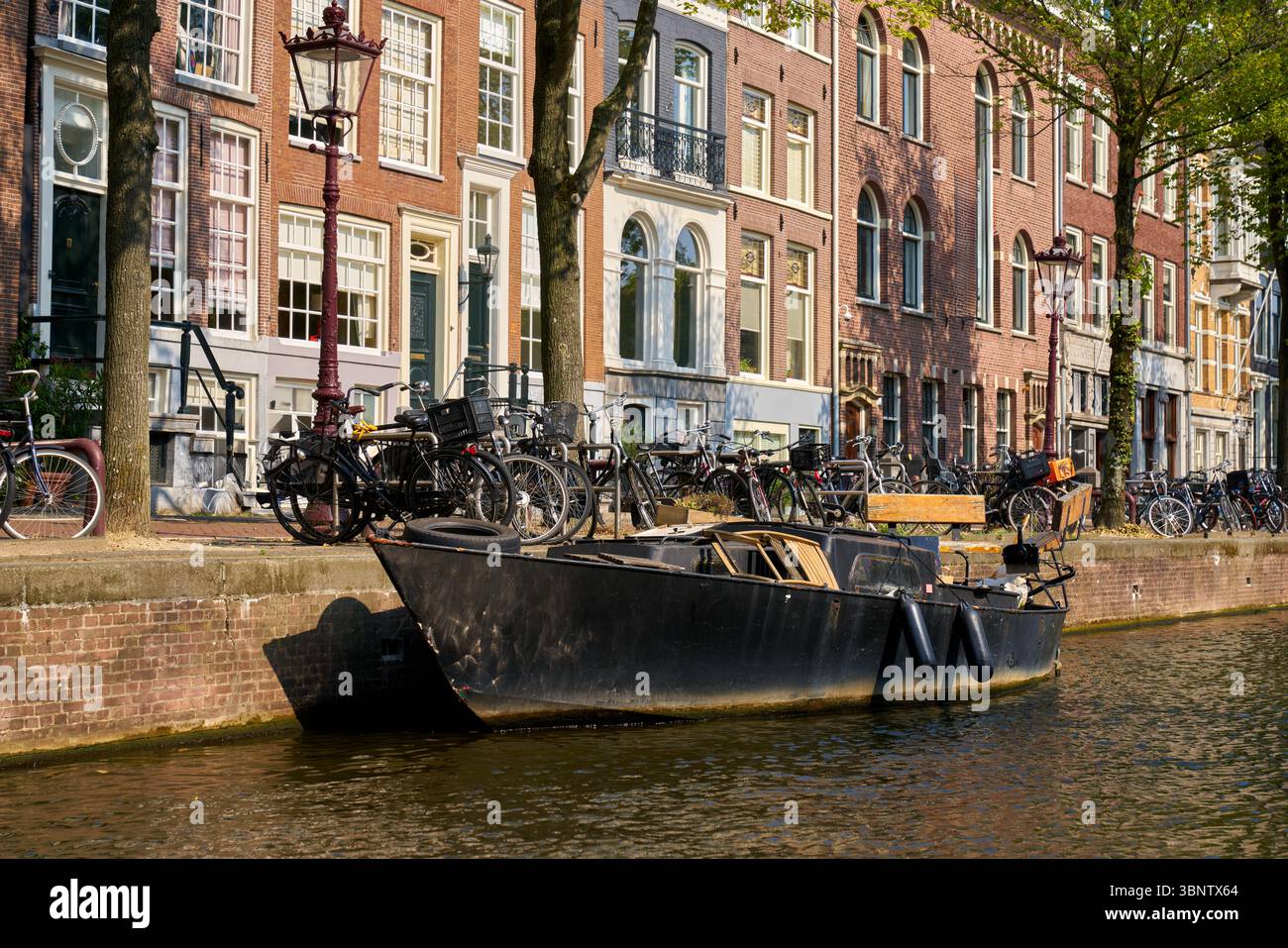Vieux bateau amarré au canal d'Amsterdam. Vieux bateau amarré sur un canal de la ville d'Amsterdam à côté d'une rue, pays-Bas. Banque D'Images
