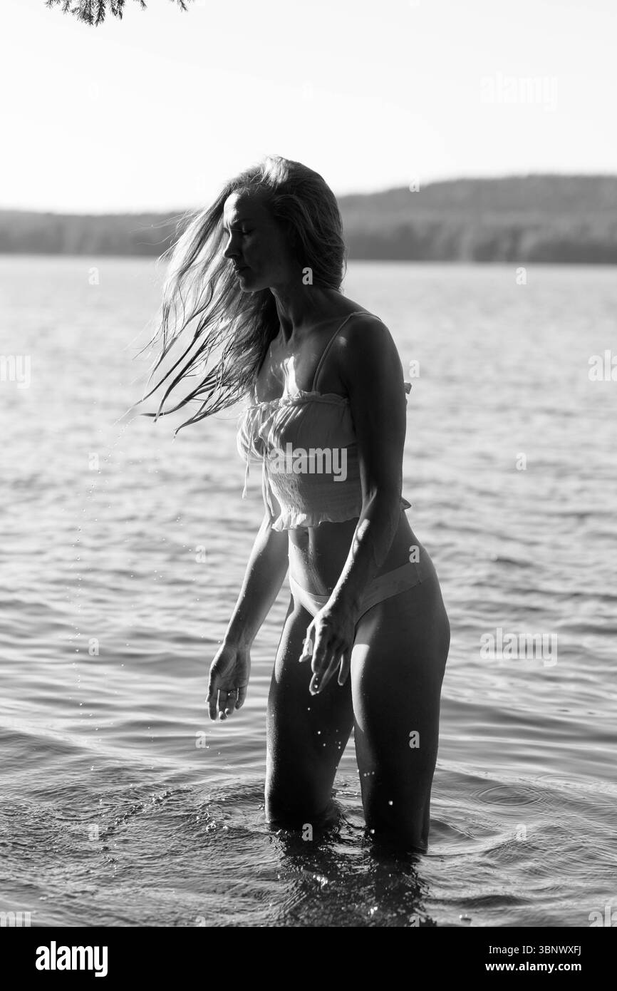 femme se tient dans l'eau peu profonde à un lac pendant une journée ensoleillée. Elle se déplace gracieusement comme des gouttelettes d'eau éclaboussent autour d'elle, et la lumière du soleil s'illumine Banque D'Images