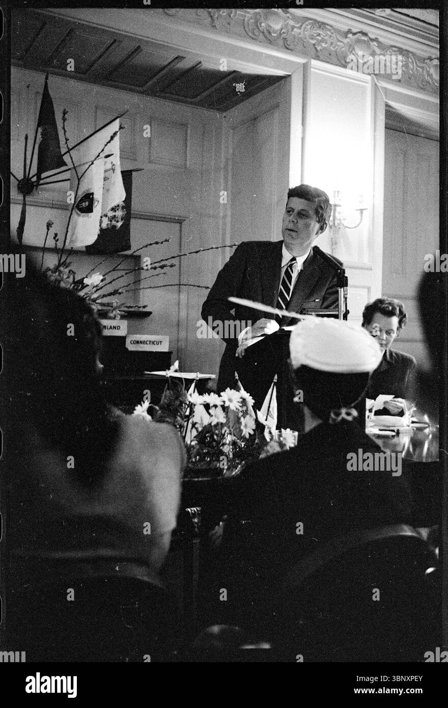 Le sénateur John F. Kennedy du Massachusetts prononce une allocution lors du déjeuner du Women’s National Democratic Club à Washington, D.C. le 13 mars 1958. Kennedy se tient sur un podium, tenant des notes, tandis que les participants écoutent attentivement dans la salle décorée. Banque D'Images