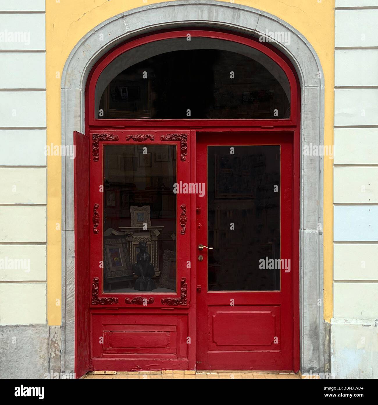 La porte arquée rouge avec des panneaux de verre ornés révèle un aperçu d'une galerie d'art vintage dans le centre historique de Varsovie. - Image de stock capturée avec un smartphone