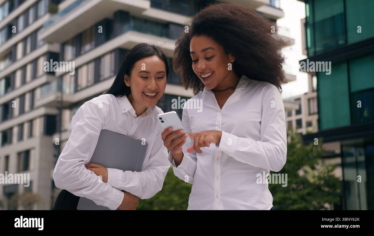 Femmes africaines asiatiques femmes d'affaires femmes d'affaires en plein air collègues multiethniques collègues tenant téléphone mobile smartphone riant sourire amusant Banque D'Images