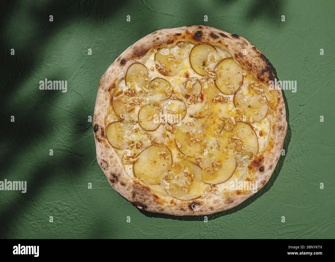 Food Still-Life, Une pizza fraîchement cuite avec de fines tranches de poire et du fromage fondu se trouve sur une surface verte vibrante. La croûte est légèrement carbonisée, enhan Banque D'Images