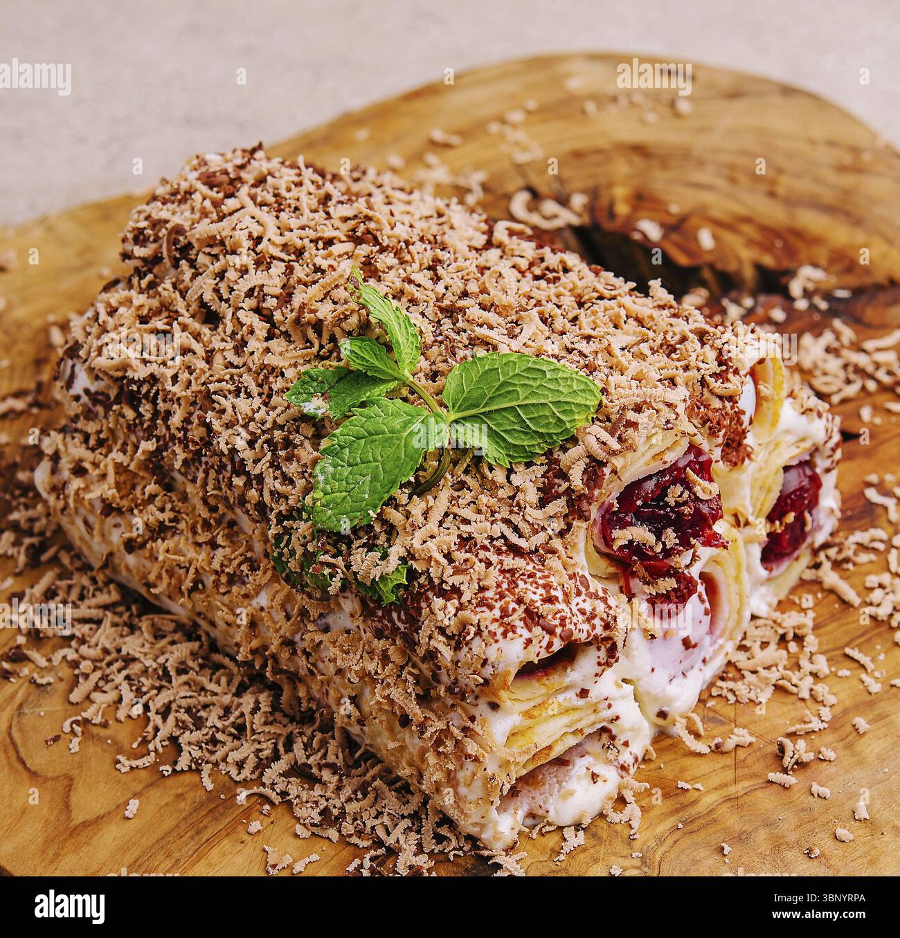 Nature morte de nourriture, gâteau à partir de crêpes roulées avec de la crème, des cerises et du chocolat râpé sur bois Banque D'Images