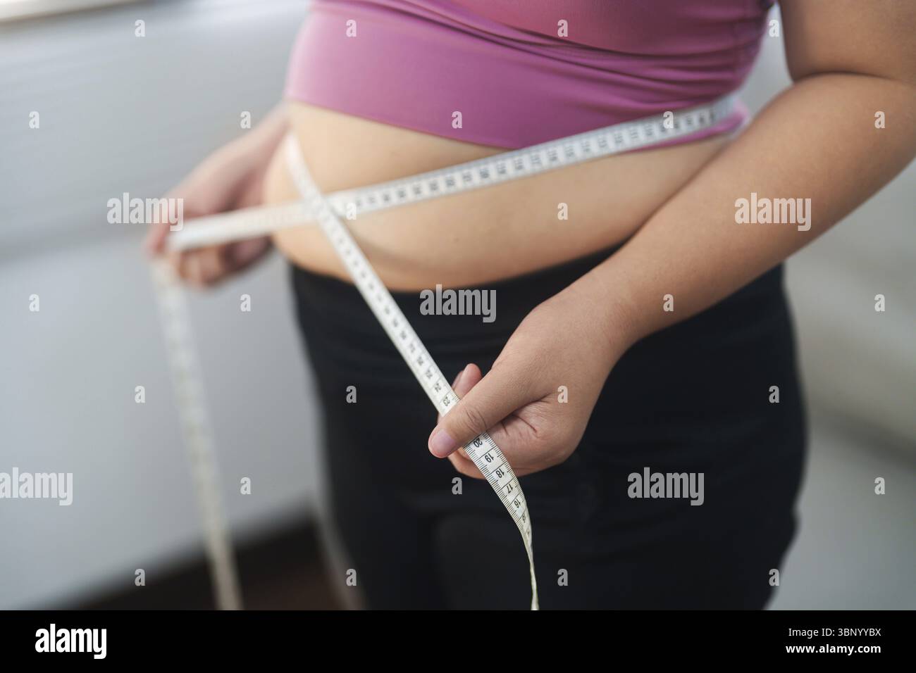 Gros plan femme en surpoids mesurant sa hanche avec ruban à mesurer Banque D'Images