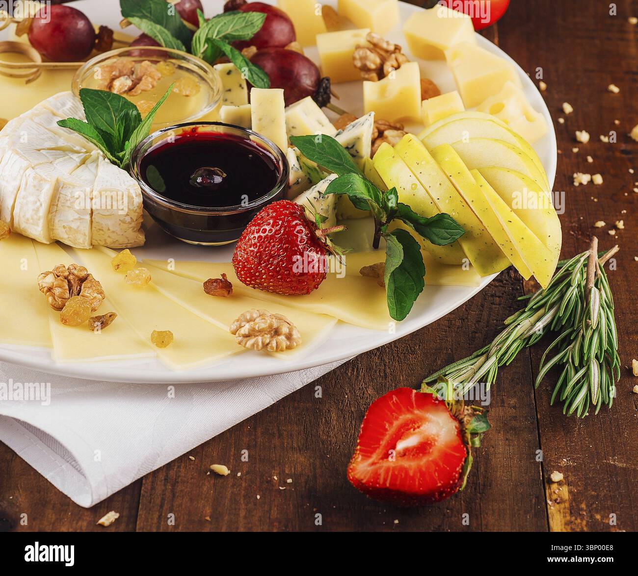 Nourriture Still-Life, assiette de fromage présentant une variété de fromages avec des fruits et des noix sur une table en bois Banque D'Images