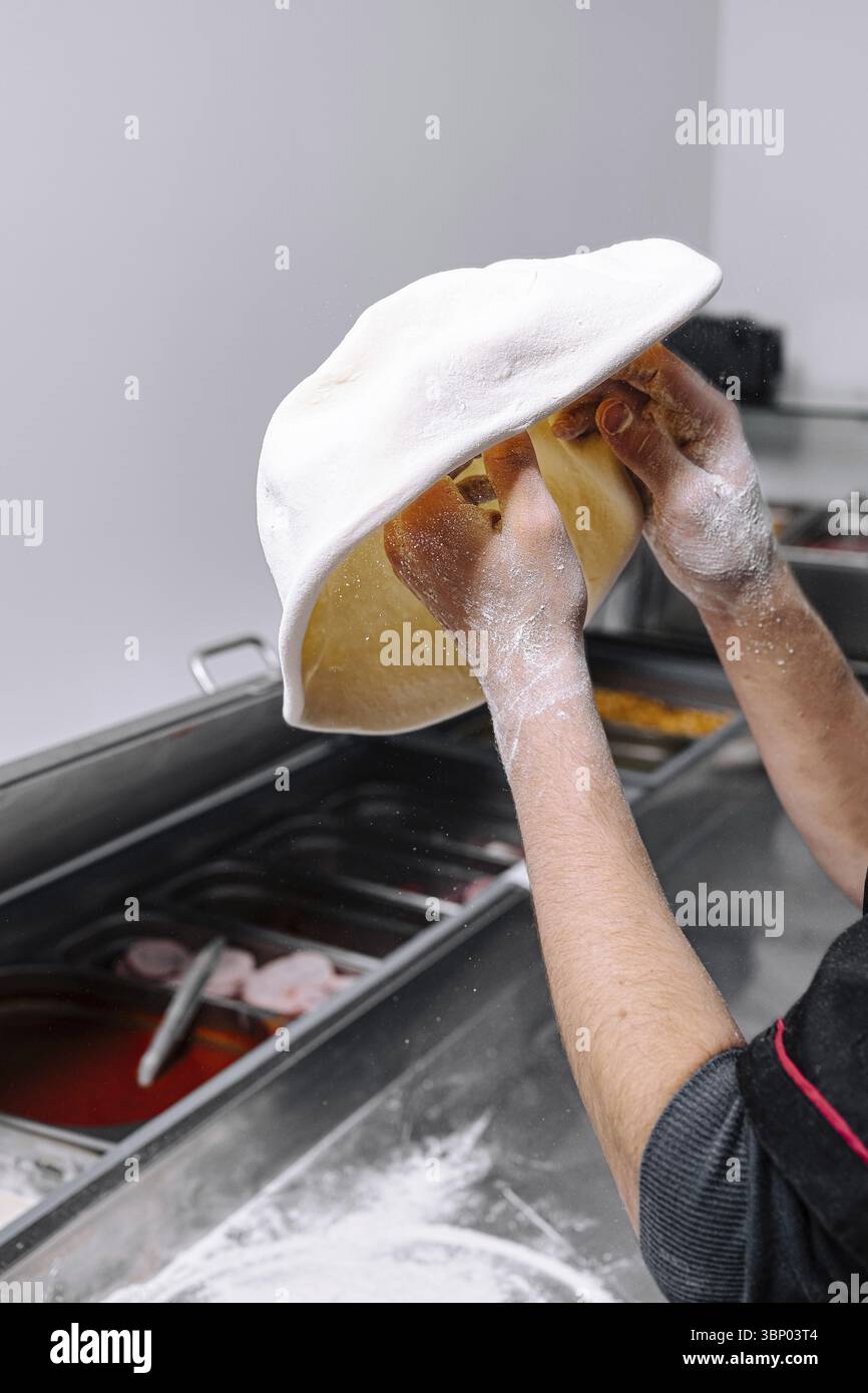 Food Still-Life, Un chef dans une cuisine animée met en valeur son expertise en jetant de la pâte à pizza fraîche dans l'air. La farine dépoussière ses mains comme le kitch Banque D'Images