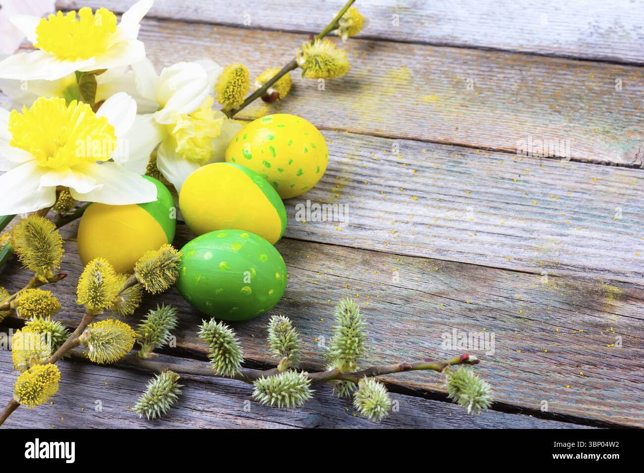 Composition de Pâques de fleurs narcisses, brindilles de saule à fleurs et oeufs de Pâques avec un motif de fleurs jaunes et vertes sur un backgroun rétro en bois Banque D'Images