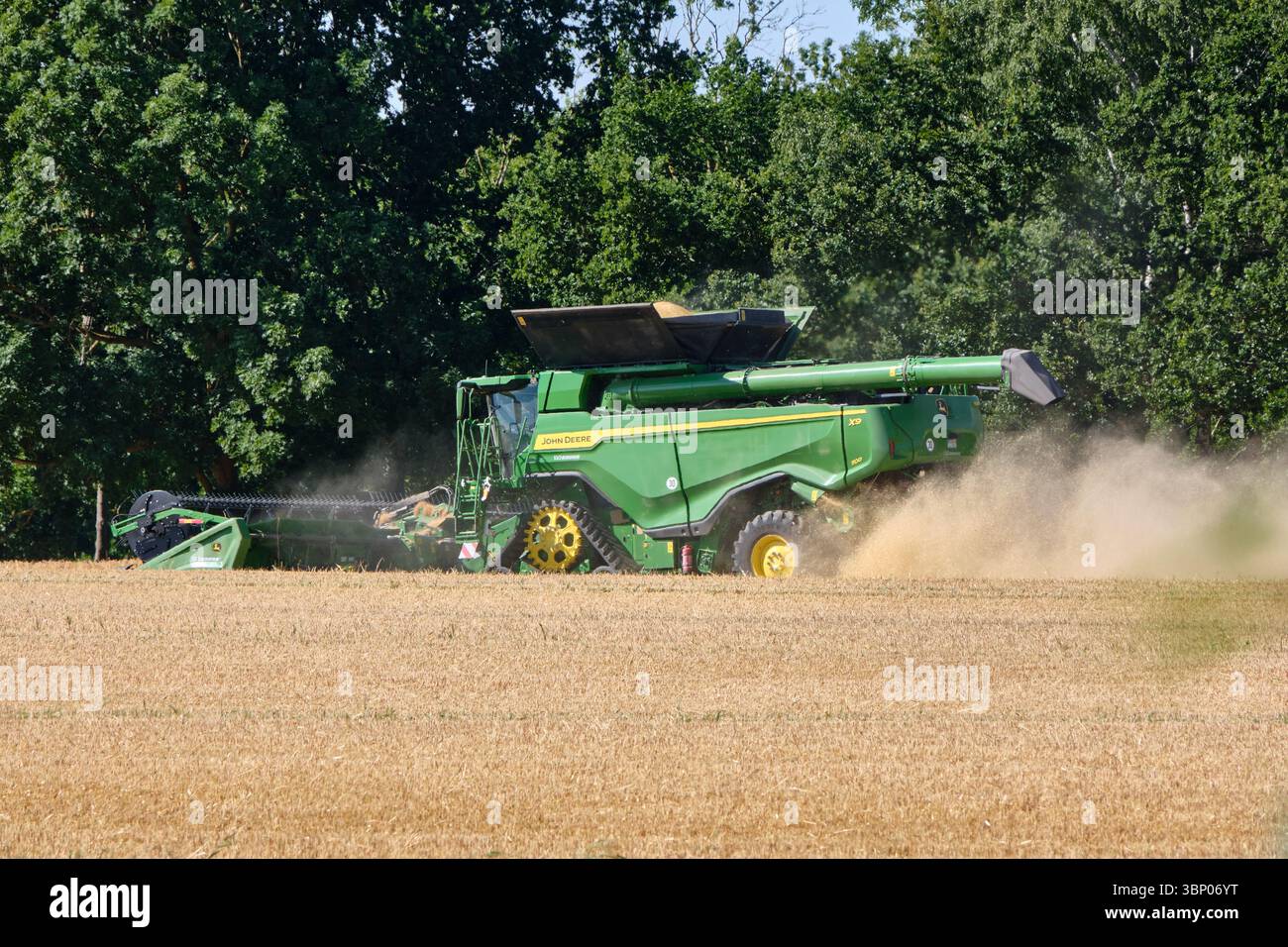 4 juillet 2025 - Lauterbach-Allemagne : une moissonneuse-batteuse John Deere travaille à travers un champ d'orge, soulevant la poussière pendant qu'elle récolte sous un ciel dégagé avec du tré Banque D'Images