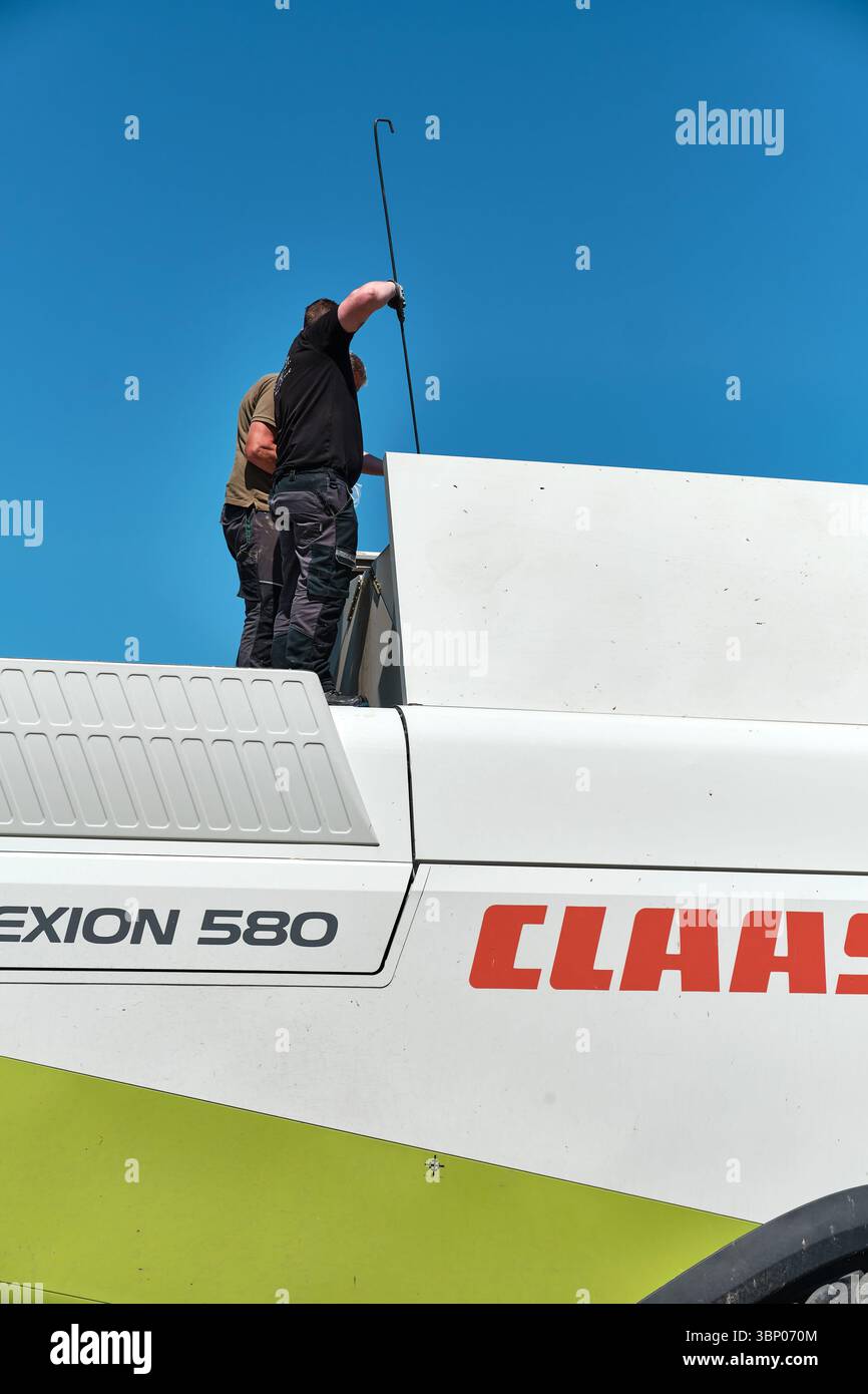4 juillet 2025 - Patzig-Allemagne : deux agriculteurs prenant un échantillon de blé d'une moissonneuse-batteuse Claas Lexion 580 sous un ciel bleu clair d'été pour voir si prod Banque D'Images