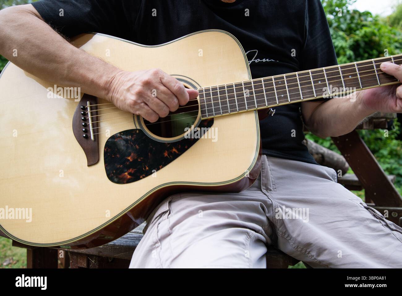 Gros plan d'un homme jouant de la guitare acoustique à l'extérieur, capturant les détails de ses mains et de son instrument à la lumière naturelle, évoquant la musique et la relaxatio Banque D'Images