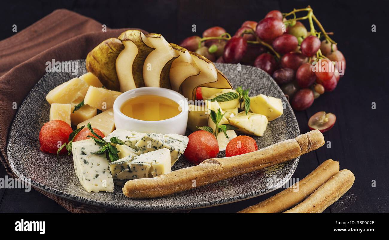 Nourriture nature morte, assiette de fromage gastronomique avec une variété de fromages, de fruits et de miel, créant une expérience visuellement attrayante et savoureuse Banque D'Images