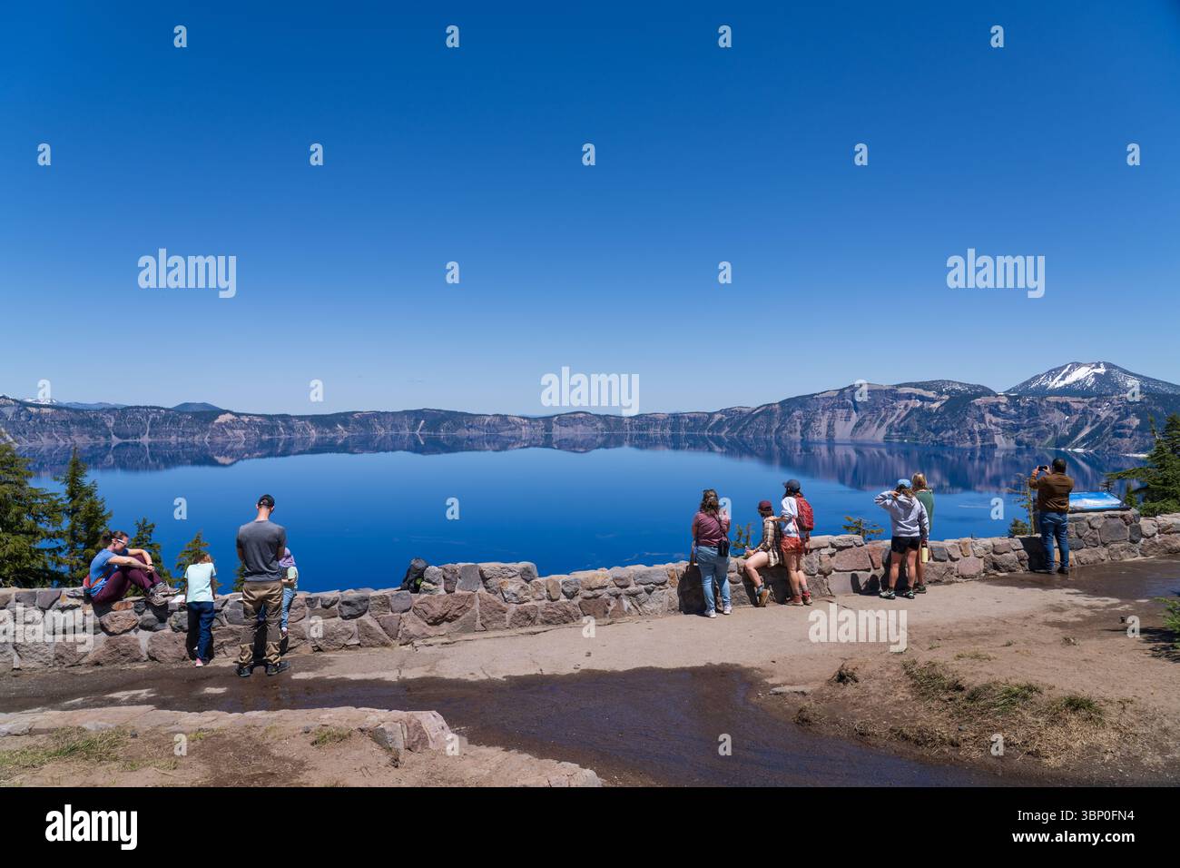 Crater Lake Rim Village South, Oregon, États-Unis - 17 juin 2025 : touristes admirant l'eau bleu profond de Crater Lake, au début de l'été, avec de la neige sur le bord Banque D'Images