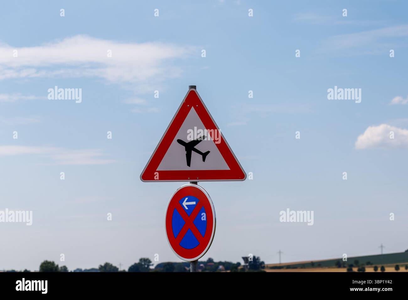 Deux panneaux de signalisation routière, un triangle et un circulaire, sont empilés sur un fond de ciel bleu et de champs et d'arbres lointains. Banque D'Images