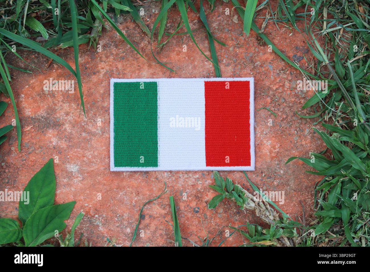 Drapeau italien brodé respectueux de l'environnement sur la pierre ancienne avec des feuilles vertes. Image symbolique pour le jour de la Terre, la conscience environnementale et le calme naturel. Banque D'Images