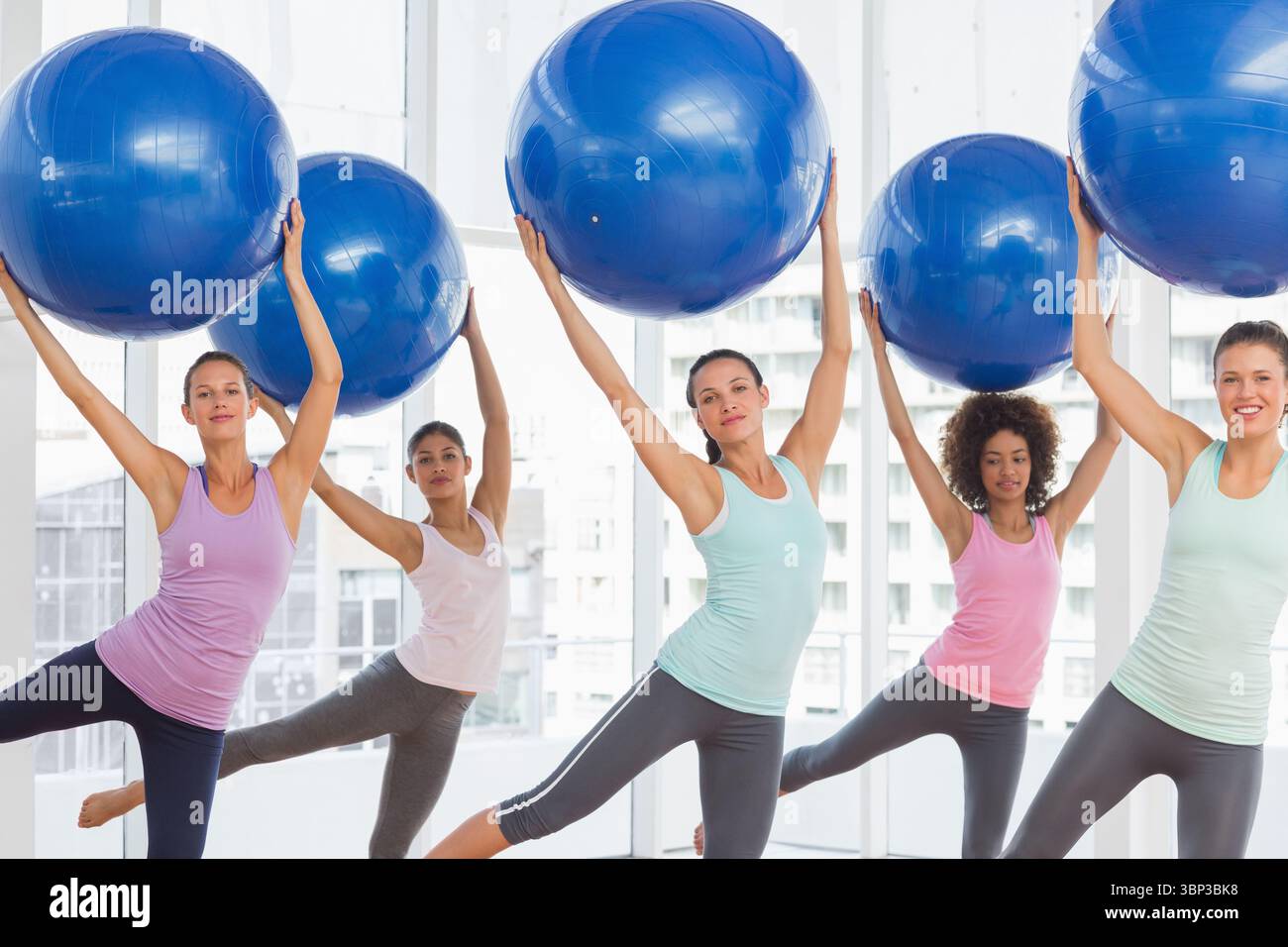 Les femmes équilibrent de grandes balles d'exercice bleues au-dessus de la tête dans un studio de fitness de conception plate, espace de copie Banque D'Images