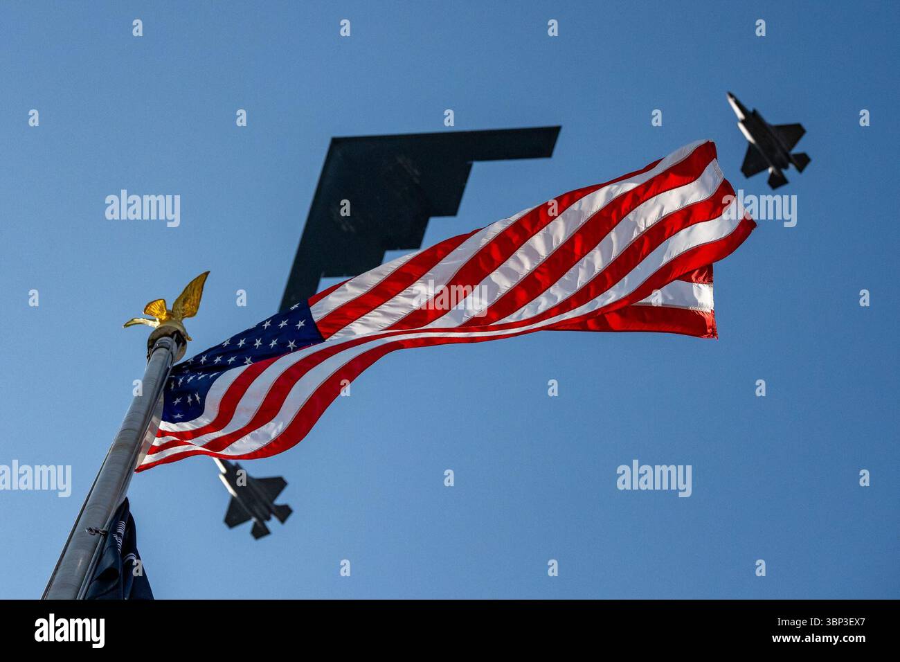 Un drapeau américain agite au sommet d'un mât à pointe d'aigle doré tandis que deux avions militaires - probablement des avions B-2 Spirit et F-35 Lightning II - volent en formation sous un ciel bleu vif, capturant une scène vivante de force patriotique et de précision aérienne pendant les célébrations du jour de l'indépendance. Washington, D.C. | 4 juillet 2025 | image reproduite avec l'aimable autorisation de la Maison Blanche. Banque D'Images
