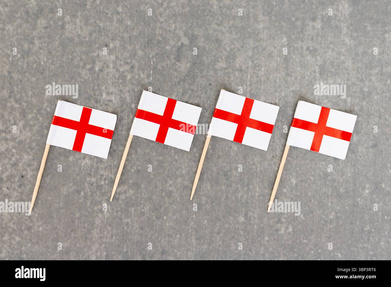 Rangée de quatre petits drapeaux Angleterre sur bâtons en bois alignés sur fond gris Banque D'Images