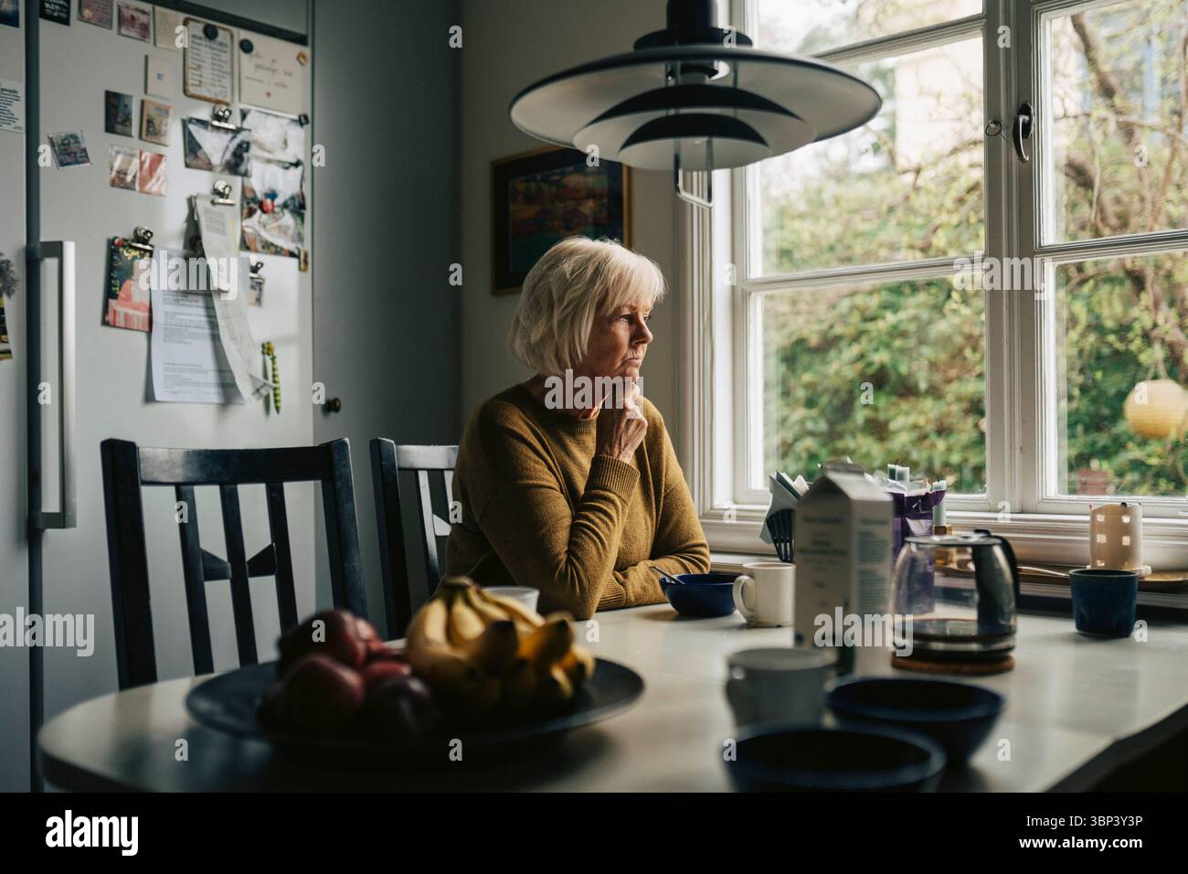 Femme âgée contemplative assise à la table à manger à la maison Banque D'Images