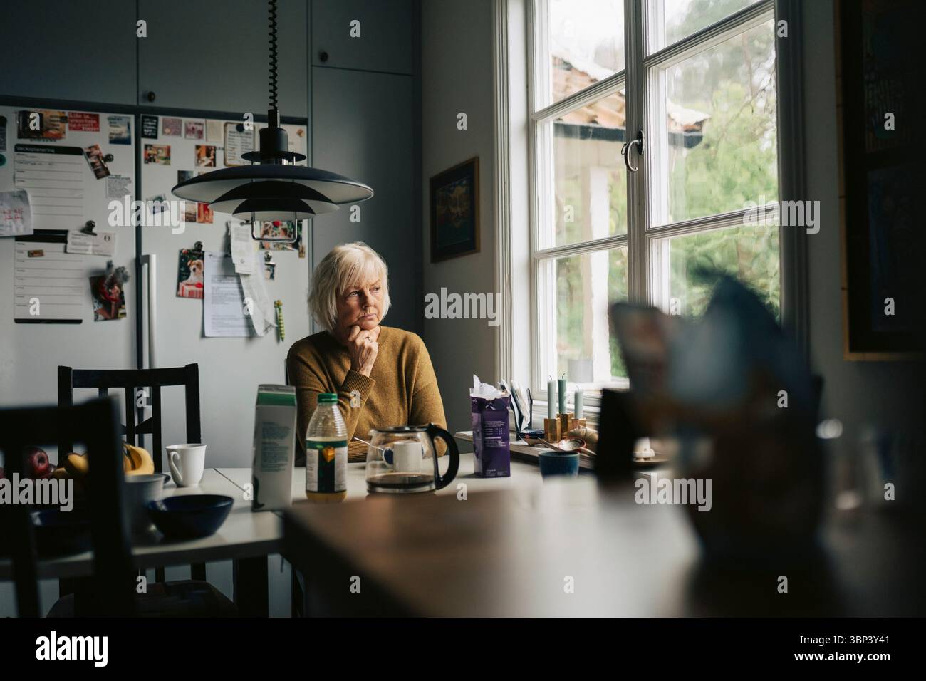 Femme senior contemplative assise à la table à manger dans la maison Banque D'Images