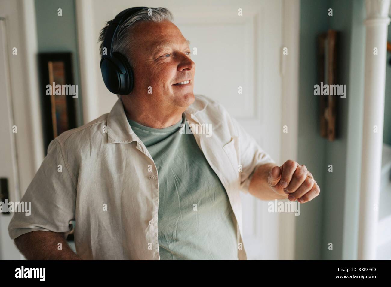 Homme âgé souriant écoutant de la musique avec des écouteurs sans fil tout en dansant à la maison Banque D'Images