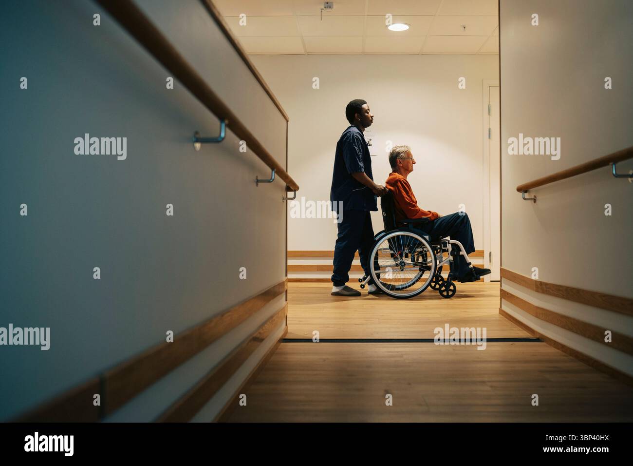 Vue latérale d'un homme âgé handicapé en fauteuil roulant dans une ruelle d'une maison de retraite Banque D'Images