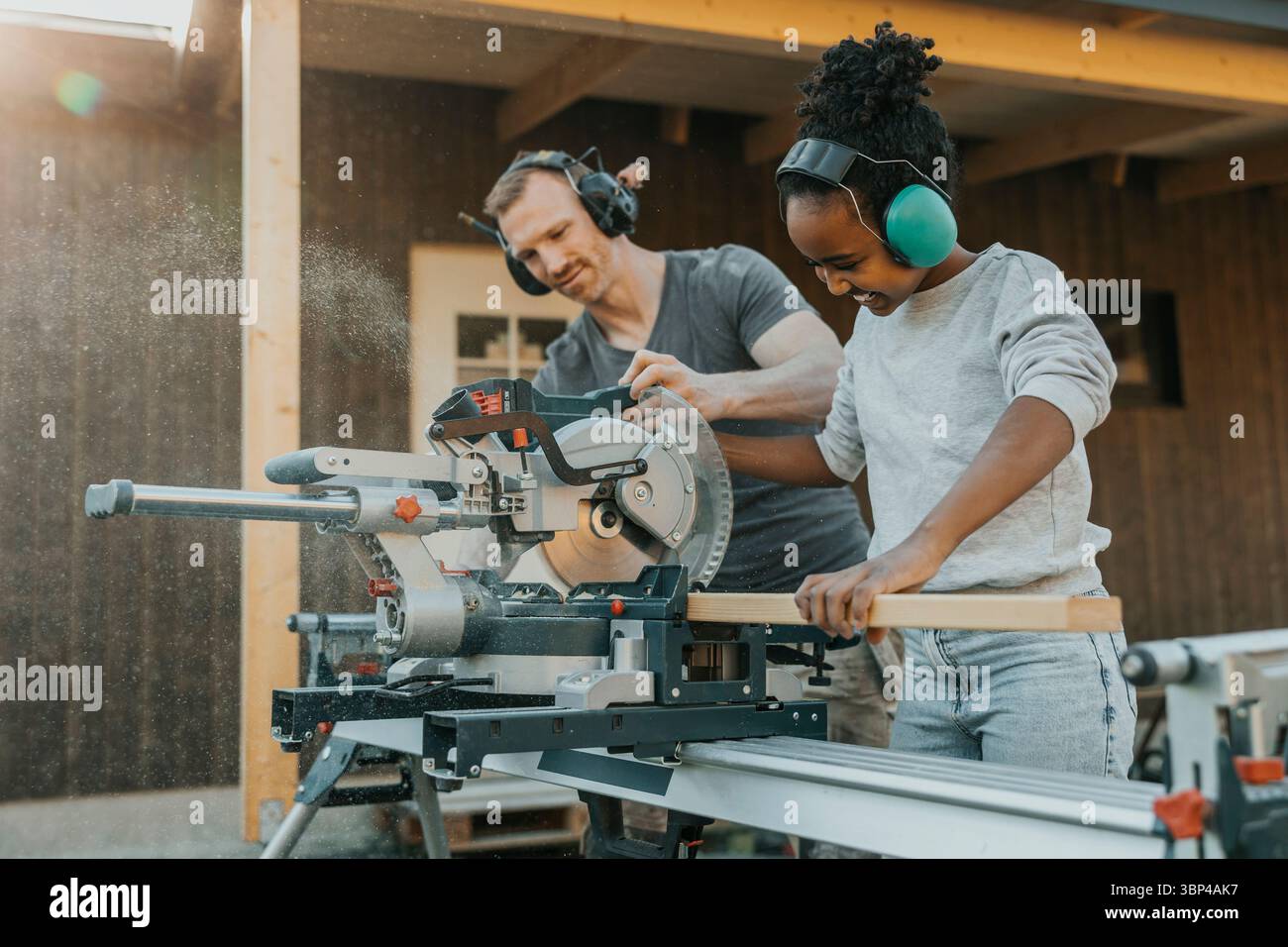 Fille aidant le père tout en coupant une planche de bois avec une scie circulaire électrique pendant la rénovation de la maison Banque D'Images