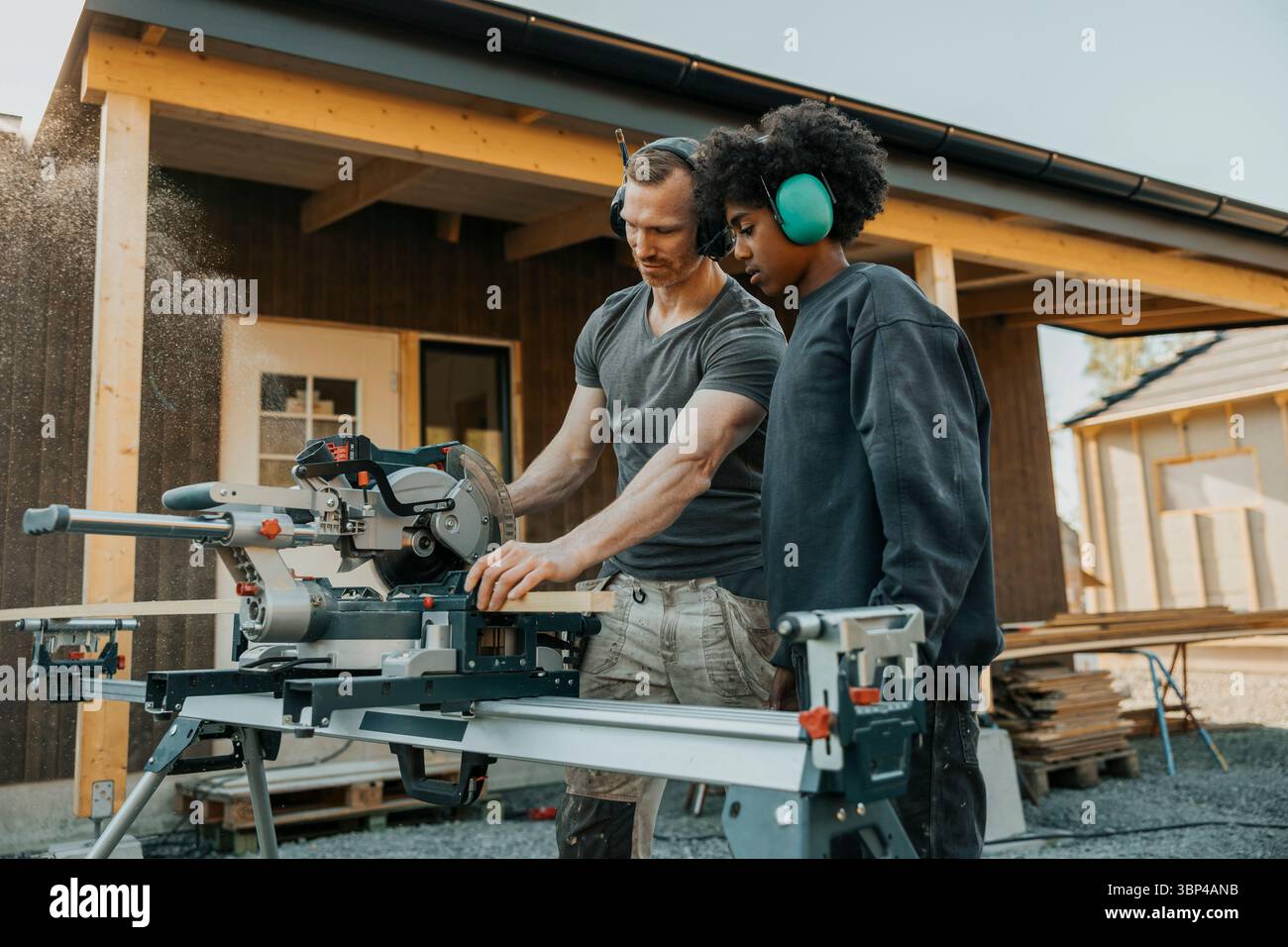 Fils portant des écouteurs à réduction de bruit regardant le père couper une planche de bois avec une scie circulaire pour la rénovation de la maison i. Banque D'Images