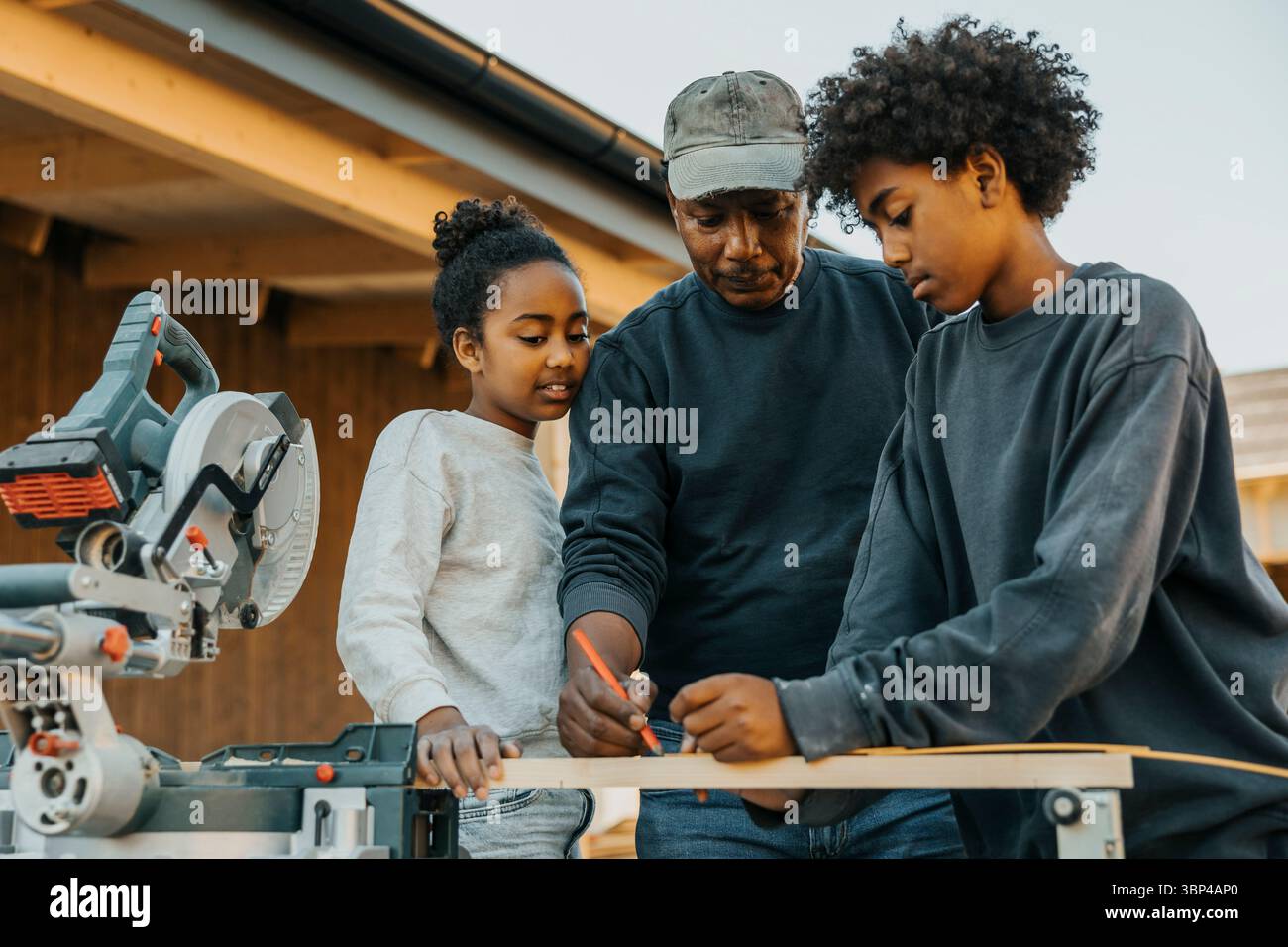 Grand-père enseignant aux petits-enfants de marquer la mesure sur une planche de bois pour la rénovation de la maison Banque D'Images