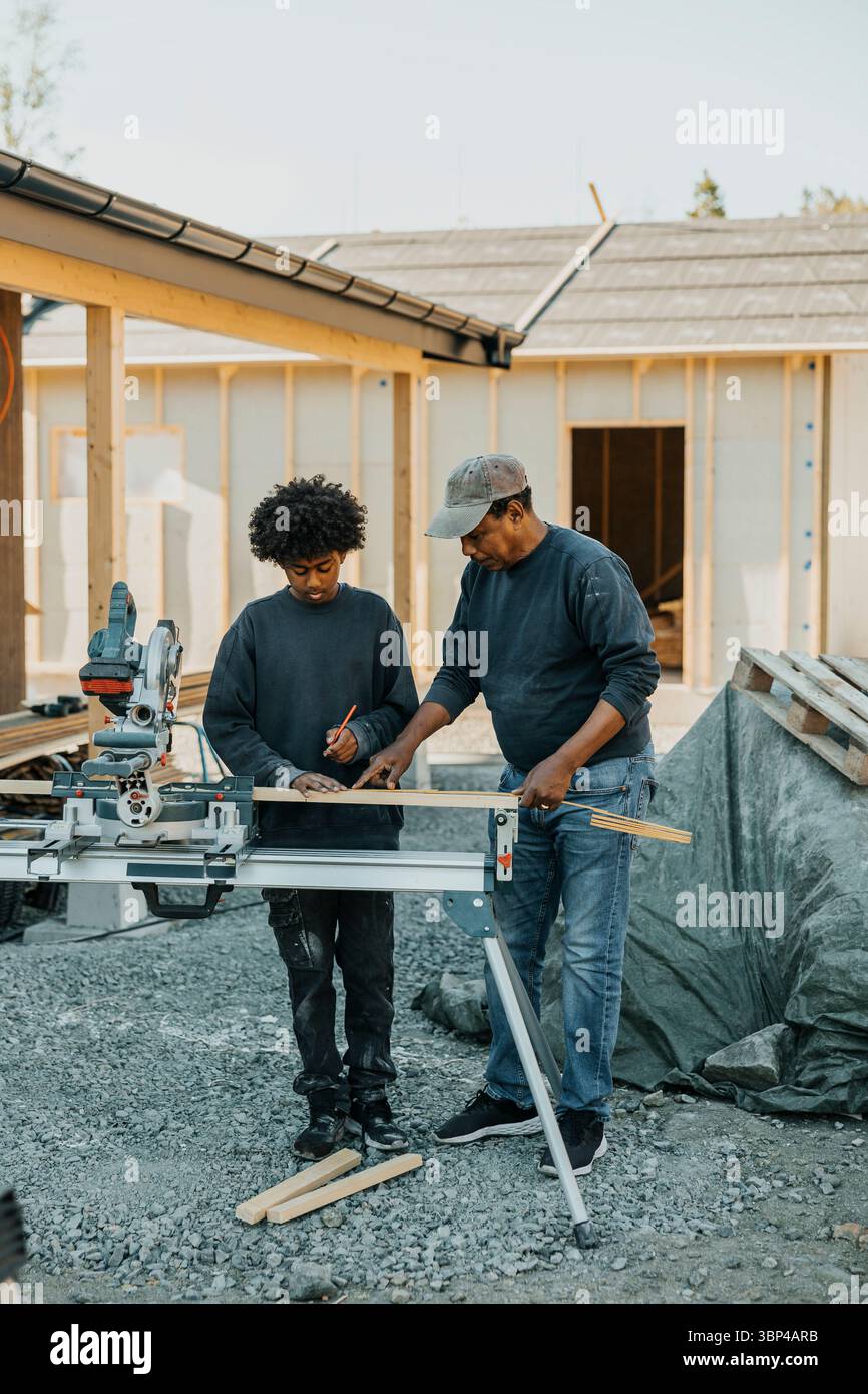 Grand-père enseignant la mesure de la planche de bois à son petit-fils tout en se tenant dans la cour arrière pour la construction de la maison Banque D'Images