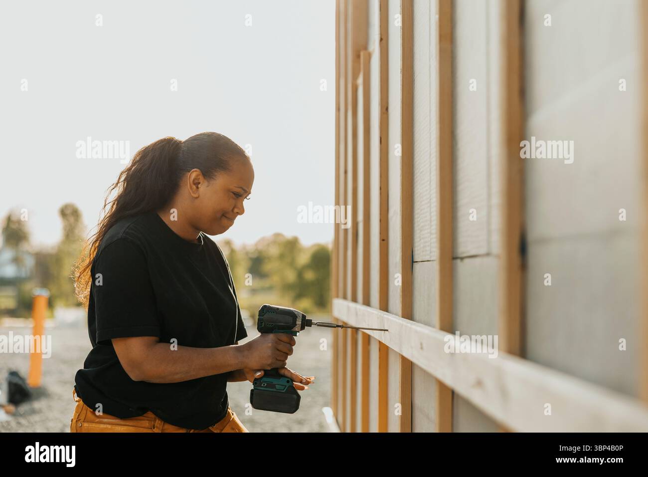 Clou de forage de menuisier féminin concentré sur planche de bois à l'extérieur de la maison Banque D'Images