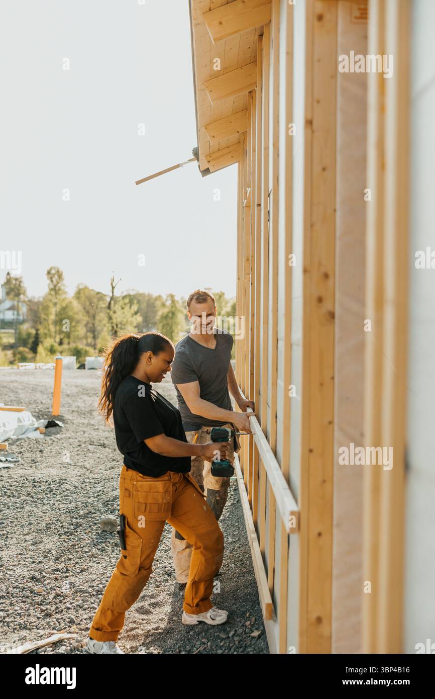 Femme perçant la planche de bois à l'extérieur de la maison avec l'aide de l'homme Banque D'Images