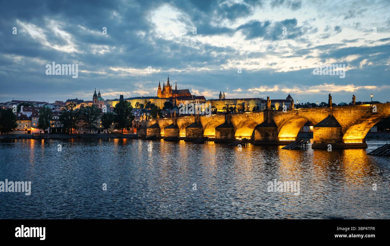 Illuminé le pont Charles et le château de Prague au coucher du soleil avec l'eau réfléchissante Banque D'Images