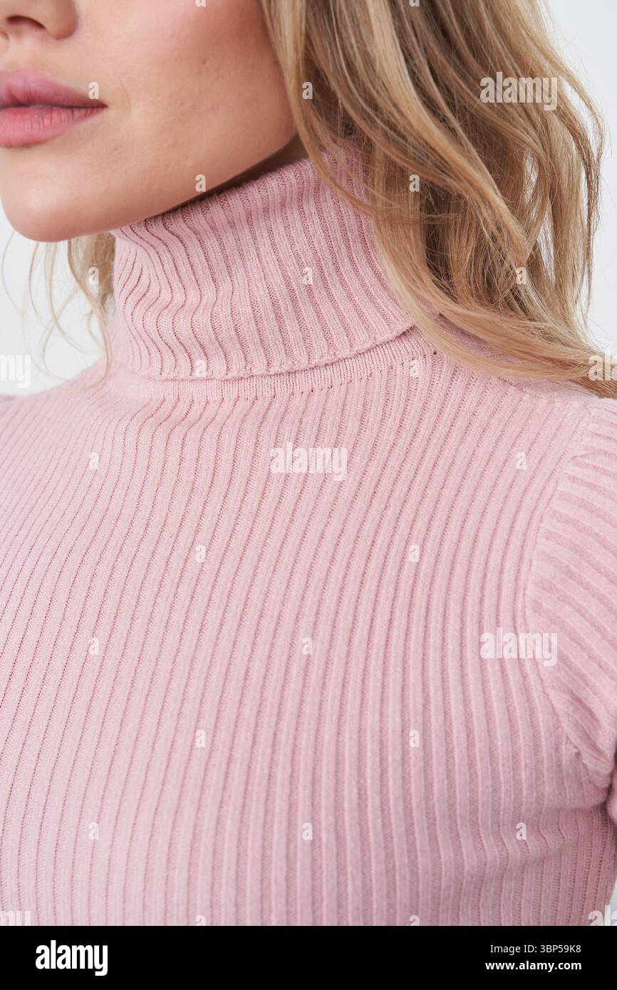 Gros plan d'une personne portant un pull à col roulé côtelé rose, montrant un profil latéral avec des cheveux longs et ondulés. La texture du tissu et le détail du col sont Banque D'Images