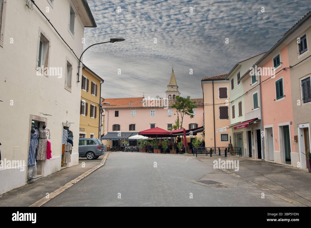 Porec, Croatie - 21 mai 2025 : rue médiévale historique avec boutiques et restaurants dans la vieille ville avec l'église notre-Dame des Anges en arrière-plan Banque D'Images