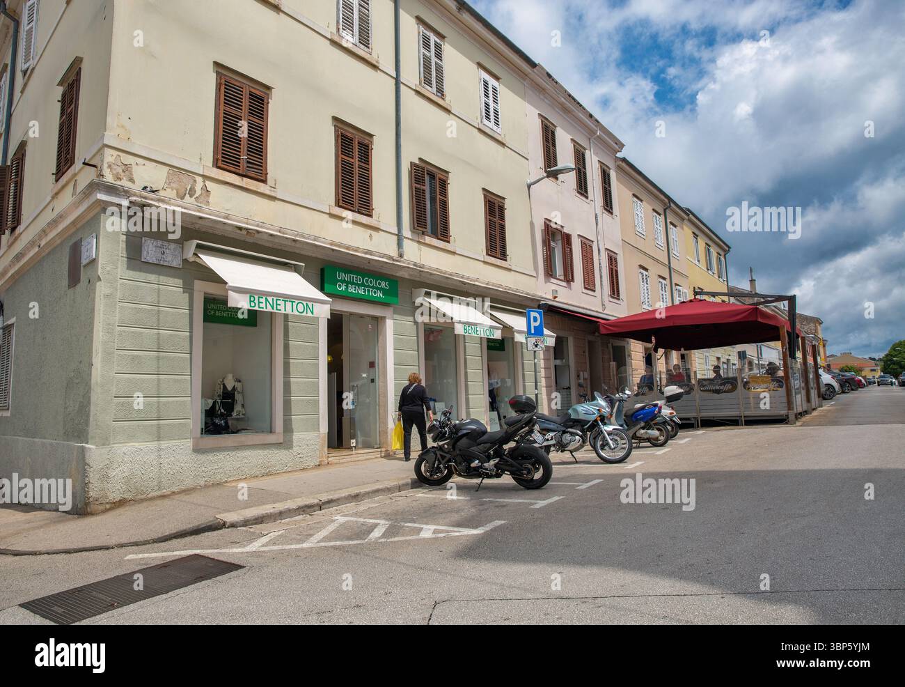 Porec, Croatie - 21 mai 2025 : rue historique dans la vieille ville avec l'architecture traditionnelle d'Istrie avec magasin de vêtements Benetton, motos garées Banque D'Images