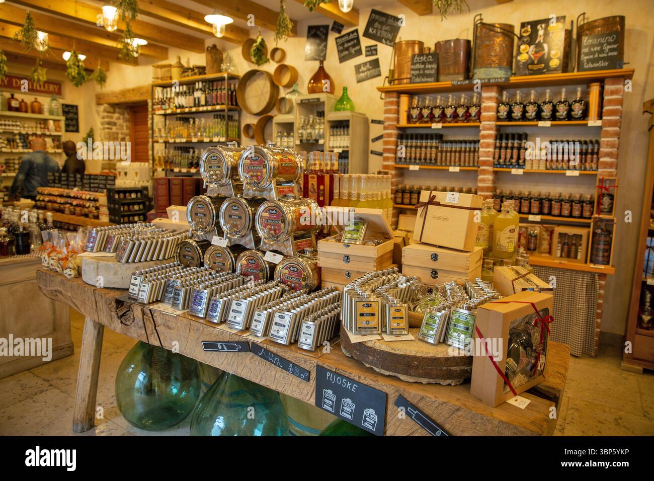 Motovun, Croatie - 22 mai 2025 : un intérieur rustique d'une boutique croate, présentant une grande table en bois chargée de vin local soigneusement arrangé, spiritueux, Banque D'Images