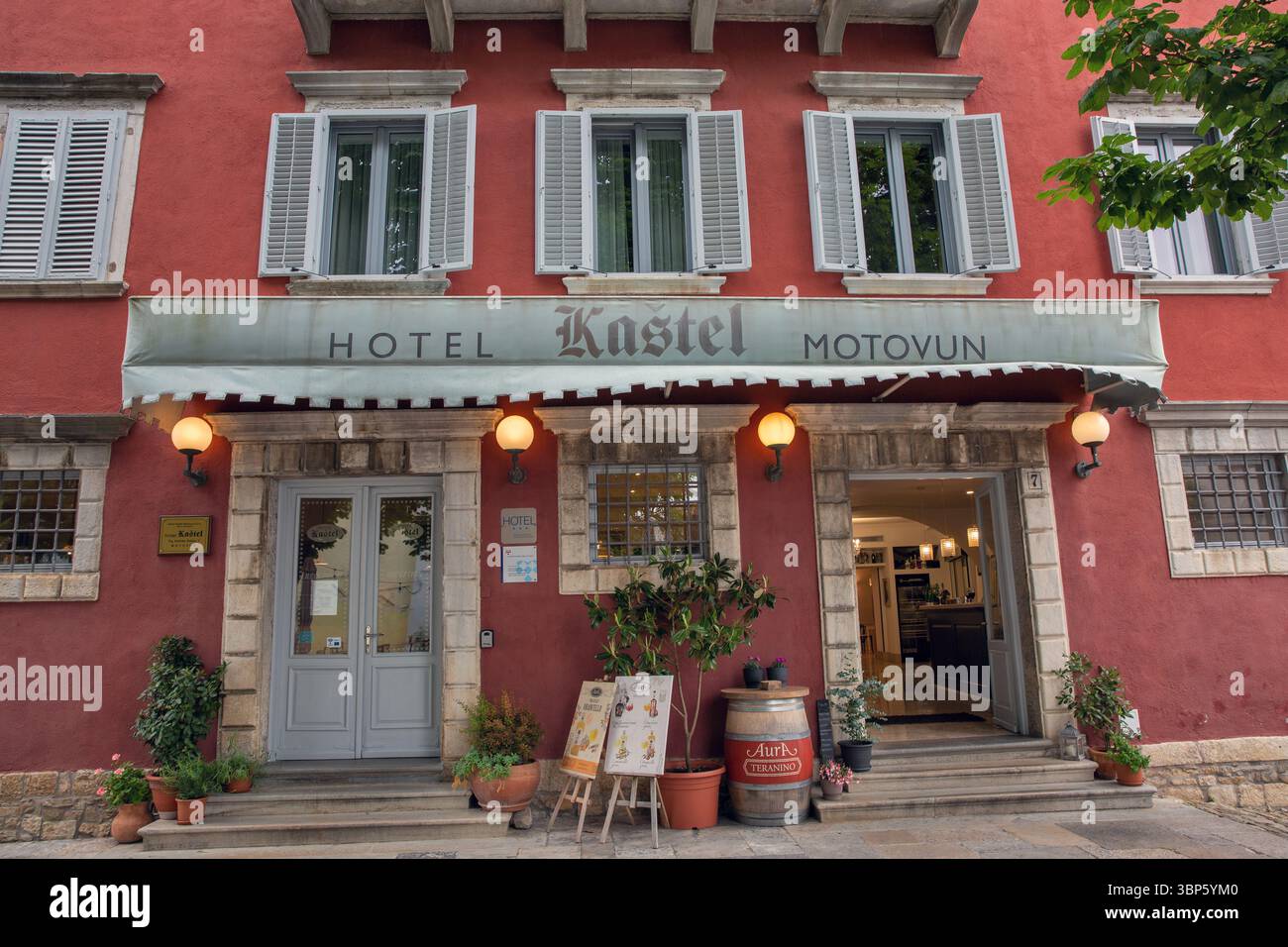 Motovun, Croatie - 22 mai 2025 : la belle façade rouge de l'Hôtel Kastel, avec des fenêtres classiques avec volets, une entrée accueillante et extérieur Banque D'Images