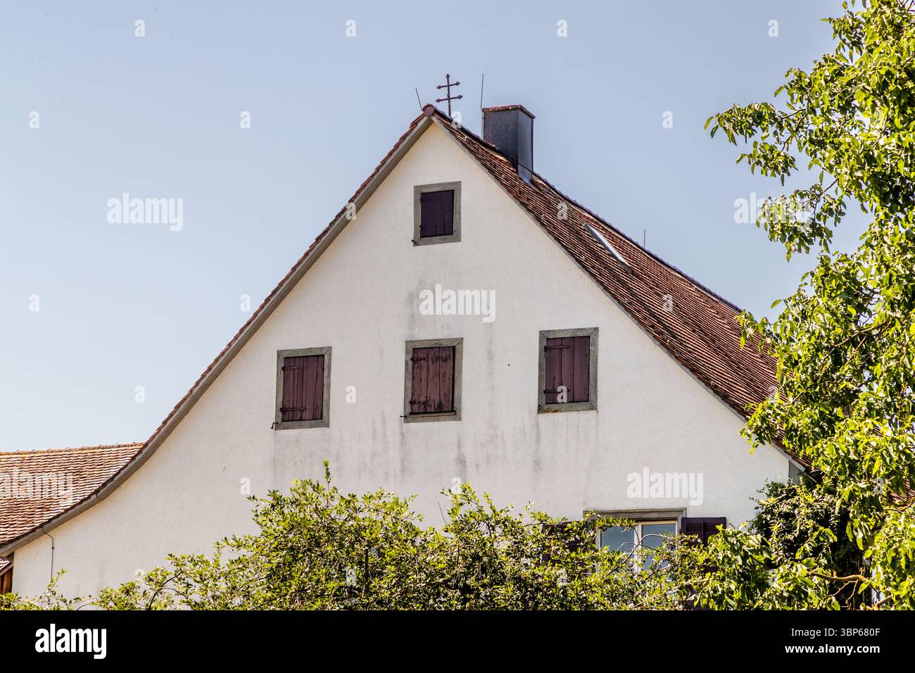 Ancienne ferme sur l'île monastère de Reichenau. Une double croix se dresse sur le pignon, signe qu'il s'agit d'un domaine féodal appartenant au monastère. La double croix est aussi un symbole de protection divine contre les tempêtes, les foudre et le feu. Cette photo montre une maison traditionnelle avec des jardins et des champs voisins à Hochwartstraße sur l'île de Reichenau dans le Bade-Württemberg, en Allemagne. La double croix sur le toit indique son statut original de domaine féodal. Il donne une impression de la vie rurale et du caractère agricole du site classé au patrimoine mondial de l'UNESCO. Hochwartstraß Banque D'Images