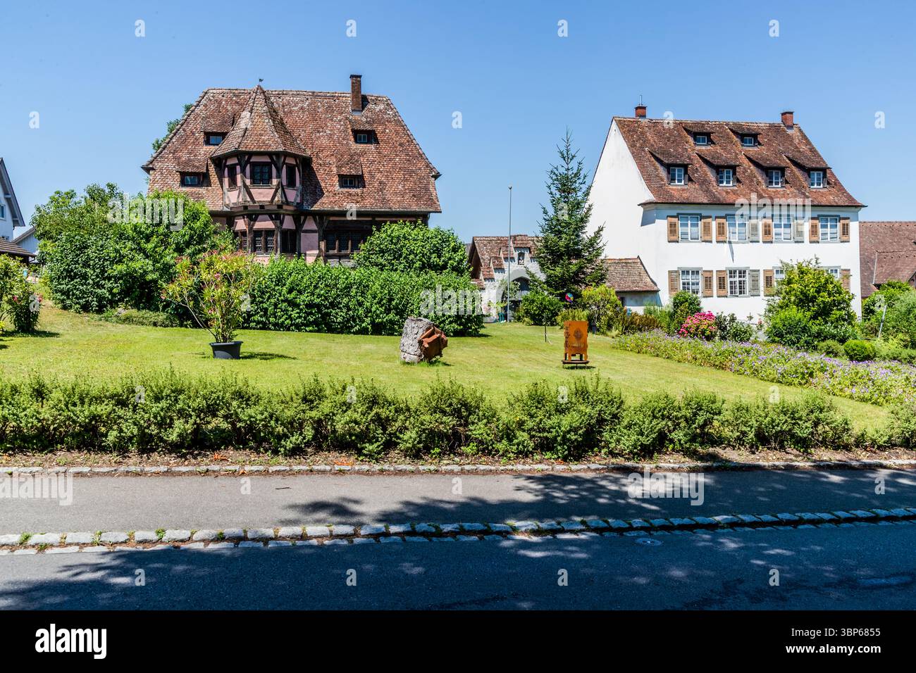 Maison à colombages avec baie vitrée ronde directement en face des magasins Mary et Mark's Minster à Mittelzell. Le bâtiment à colombages de deux étages avec une baie vitrée polygonale présente des éléments décoratifs à colombages tels que les croix d'Andrew, typiques de la tradition alémanique. Vue sur les maisons traditionnelles et les jardins entretenus à Münsterplatz sur l'île de Reichenau, en Allemagne. La scène montre l'atmosphère idyllique de ce site classé au patrimoine mondial de l'UNESCO sous un ciel bleu. Münsterplatz, Reichenau, Bade-Württemberg, Allemagne Banque D'Images